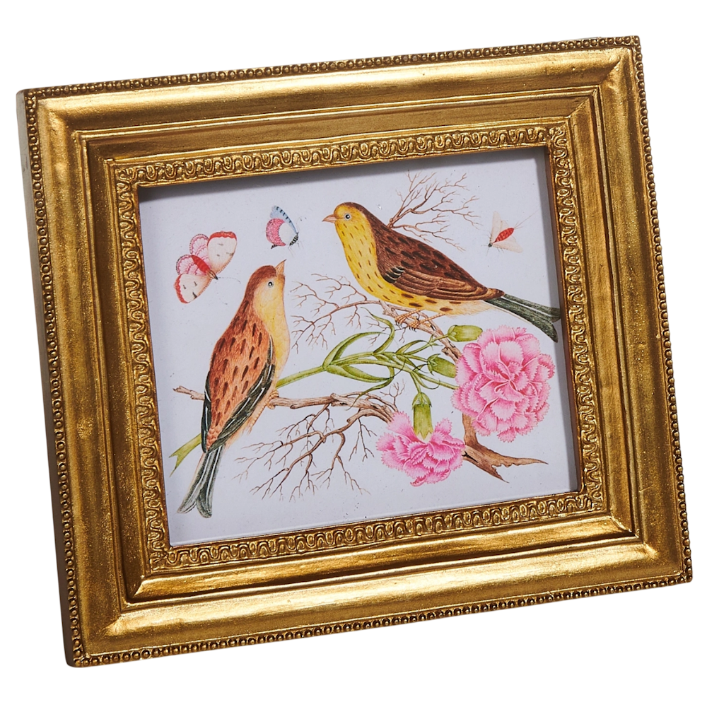 Framed artwork in a gold frame shows two birds perched on a branch with pink flowers and butterflies. The tone is vibrant and harmonious.