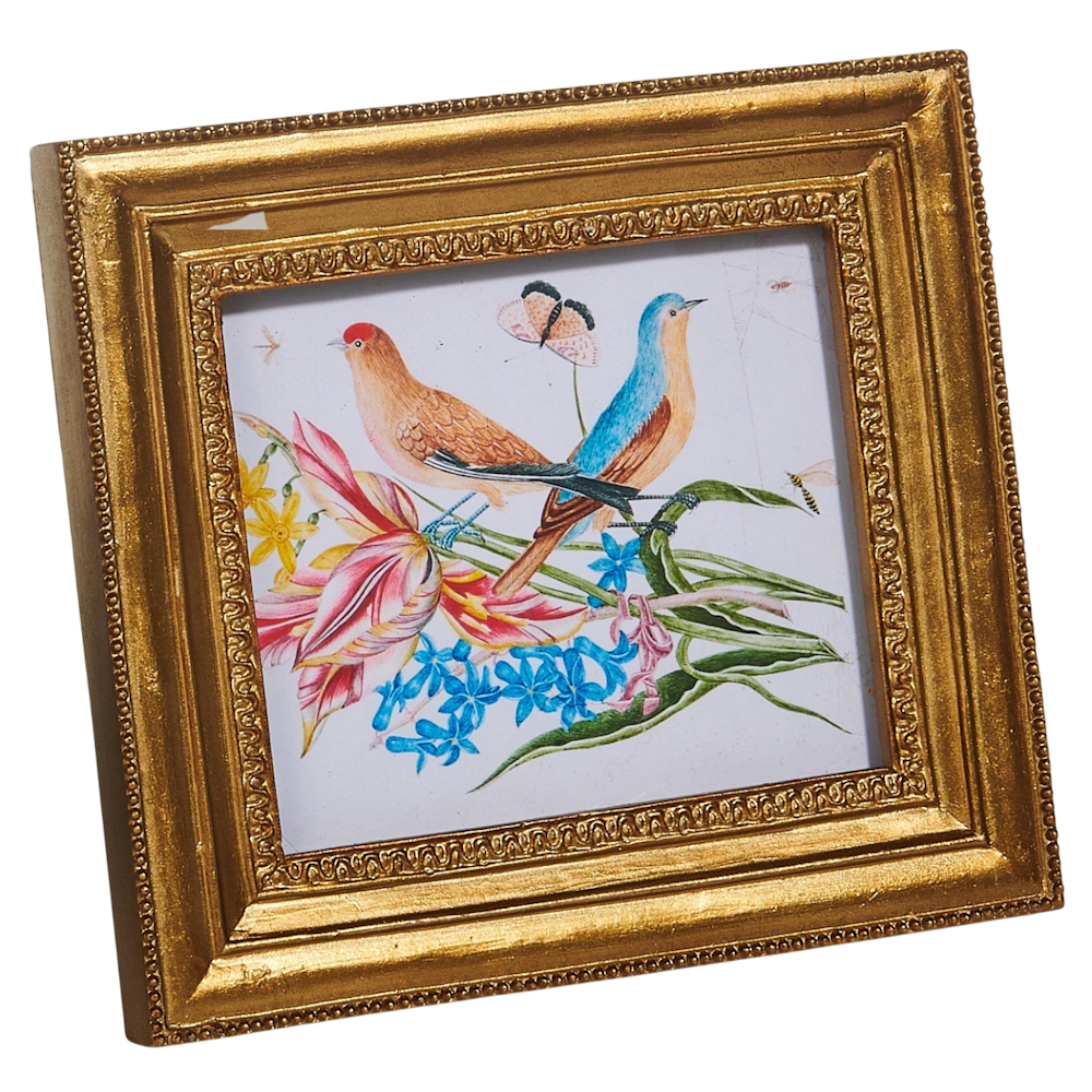 Framed artwork depicts two colorful birds perched on vibrant flowers with a butterfly overhead, set in an ornate gold frame, conveying a cheerful tone.
