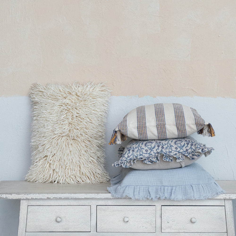 Four pillows in varied textures and patterns arranged on a rustic white dresser against a two-tone wall.