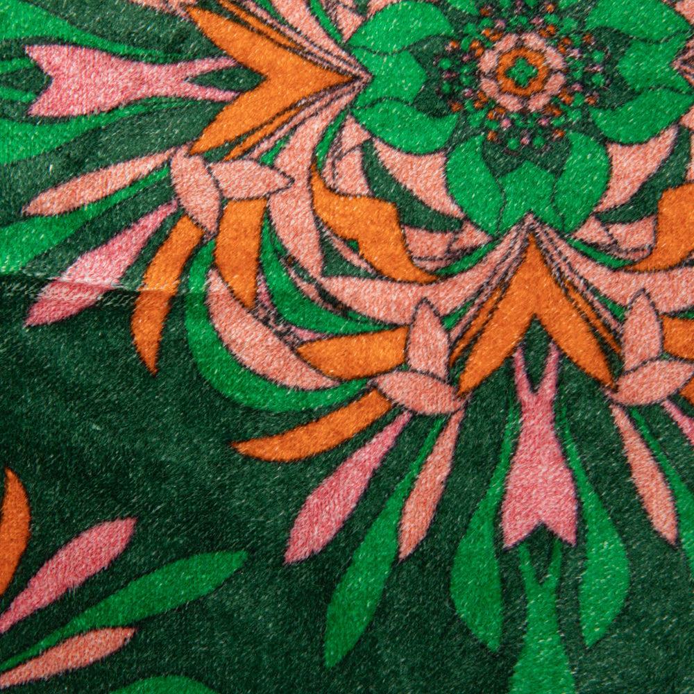 Close-up of a green velvet fabric featuring a vibrant orange, pink, and green floral mandala pattern.