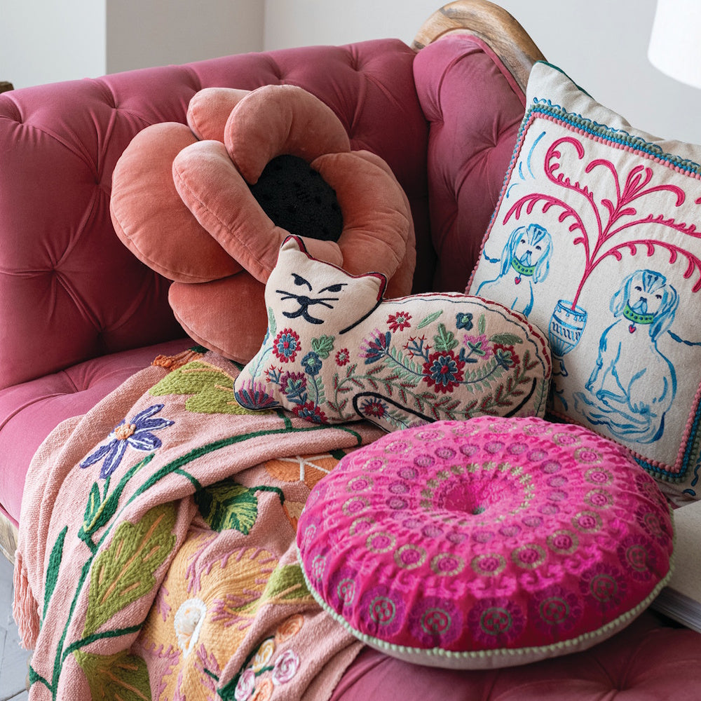 Staffordshire dog pillow, embroidered cat cushion, and boho throw blanket on a pink tufted sofa.