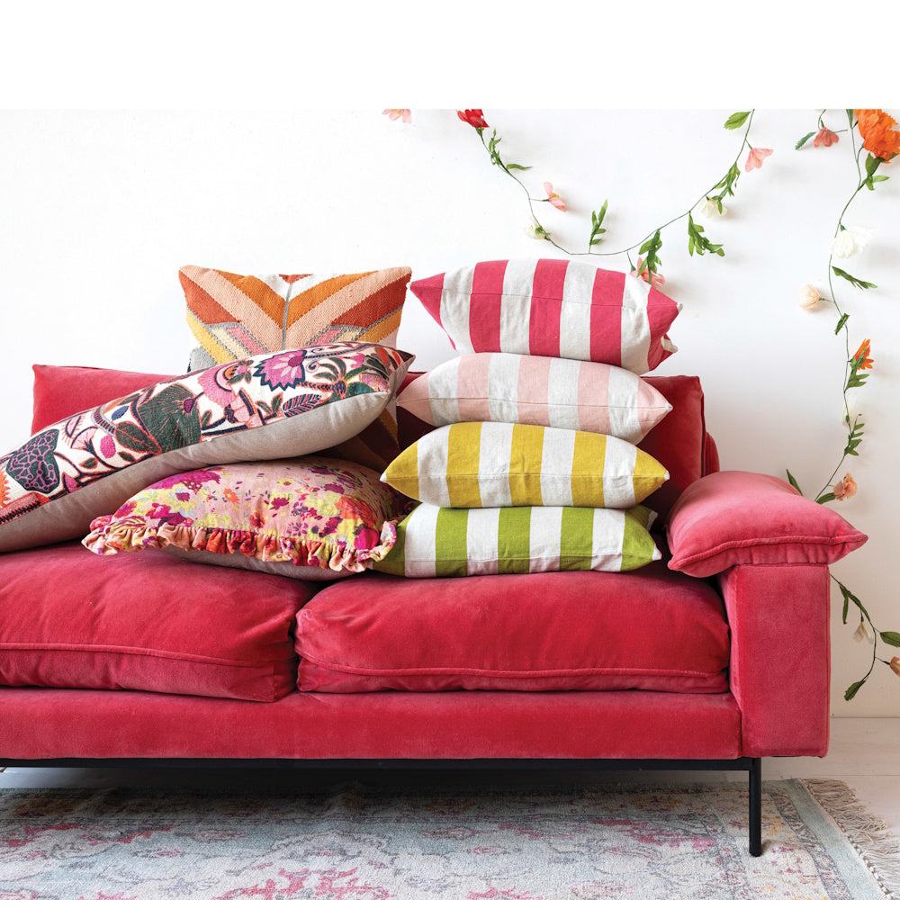 A bright pink sofa piled with a colorful variety of patterned, striped, and floral decorative throw pillows.