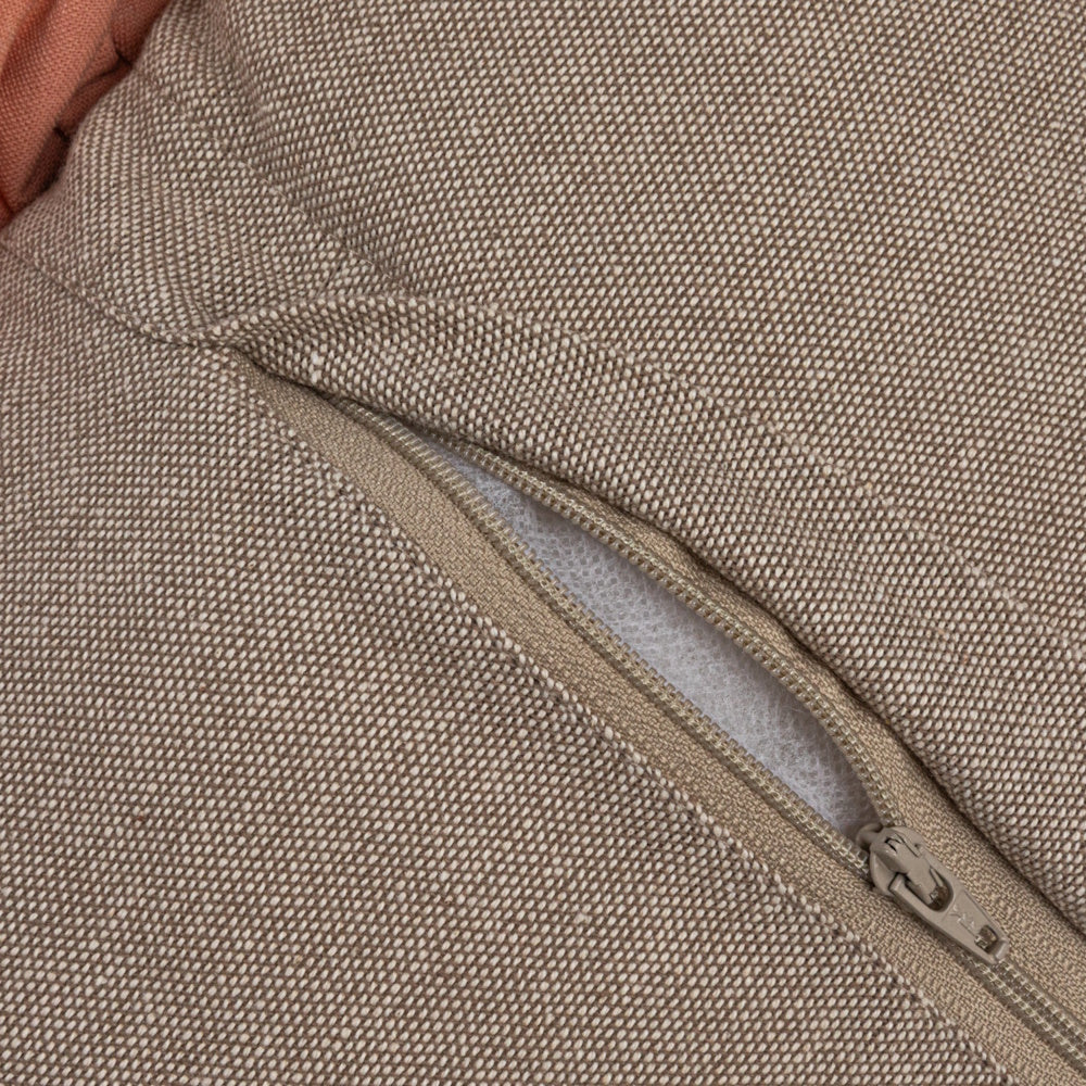 Close-up of a beige textured fabric pillow with a partially opened zipper revealing white filling inside.