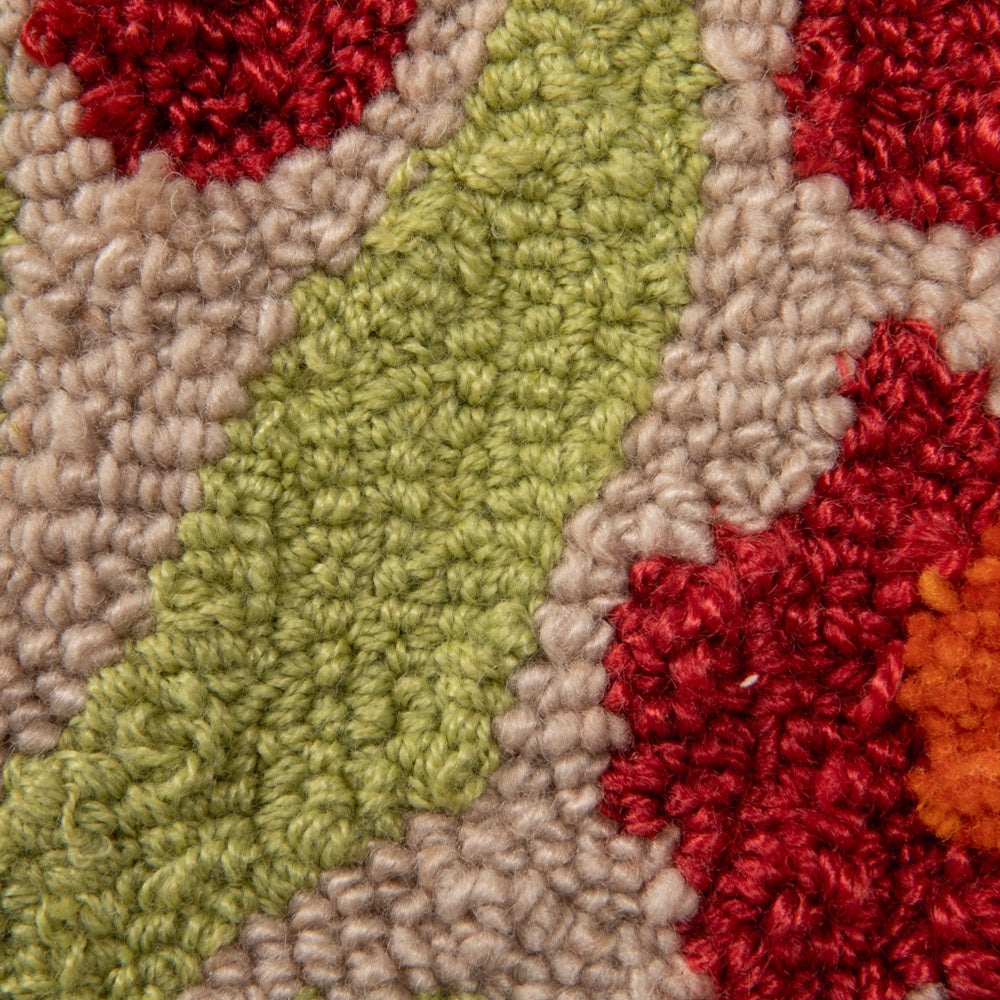 Close-up of a hooked tufted pillow showing textured loops of red, green, and beige yarn in a floral pattern.