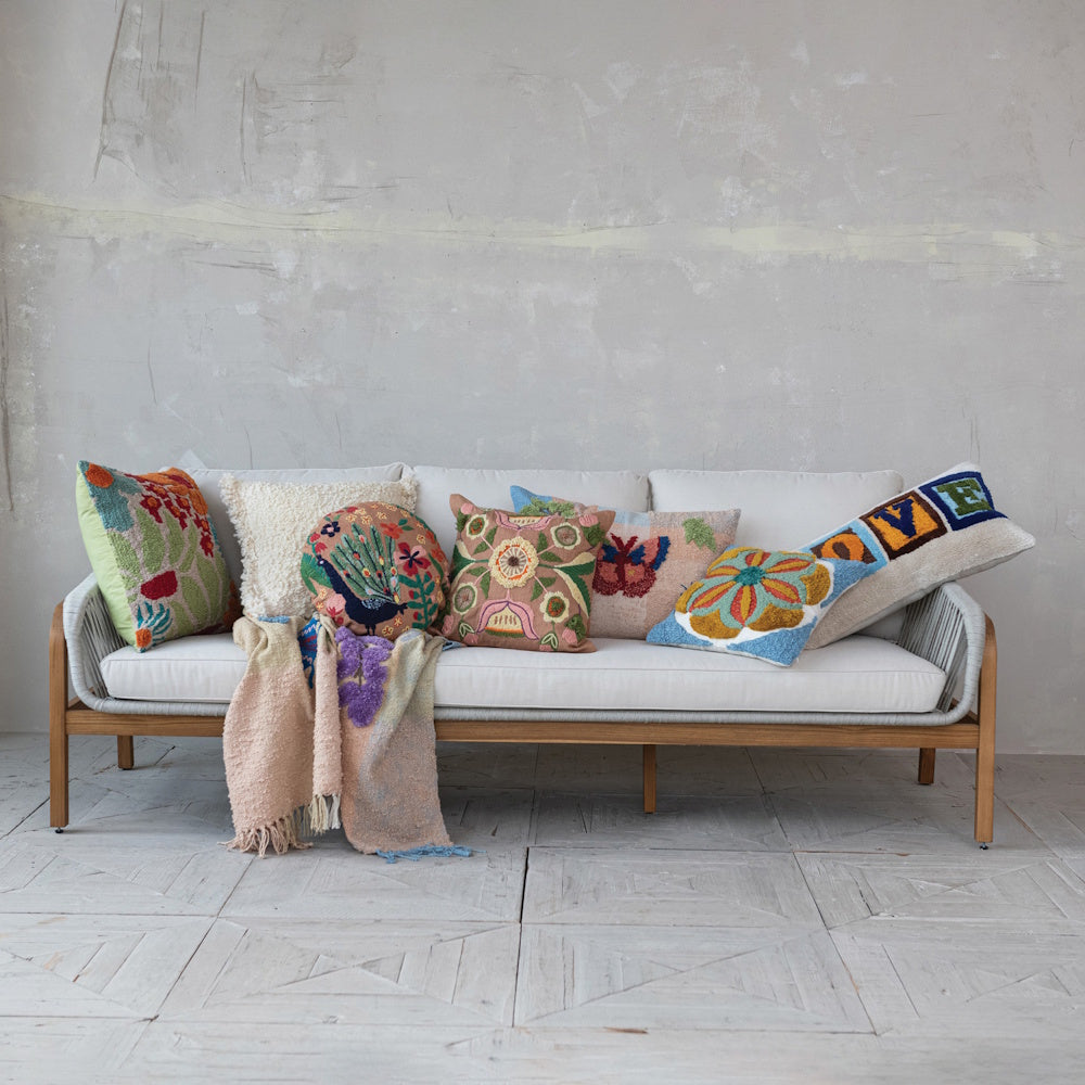 Eclectic outdoor sofa with colorful floral, peacock, and butterfly tufted pillows and a textured throw blanket.