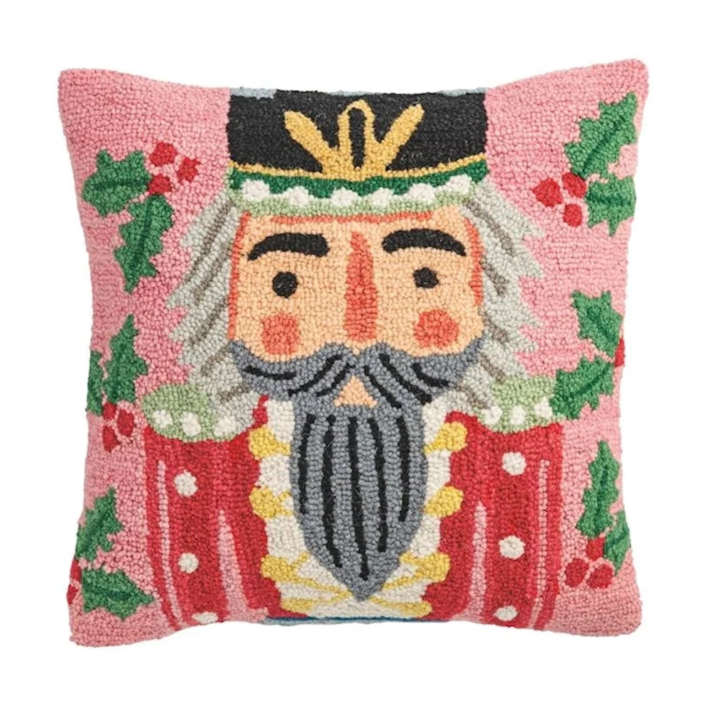 Square wool hook pillow featuring a nutcracker portrait with holly leaves against a pink background.
