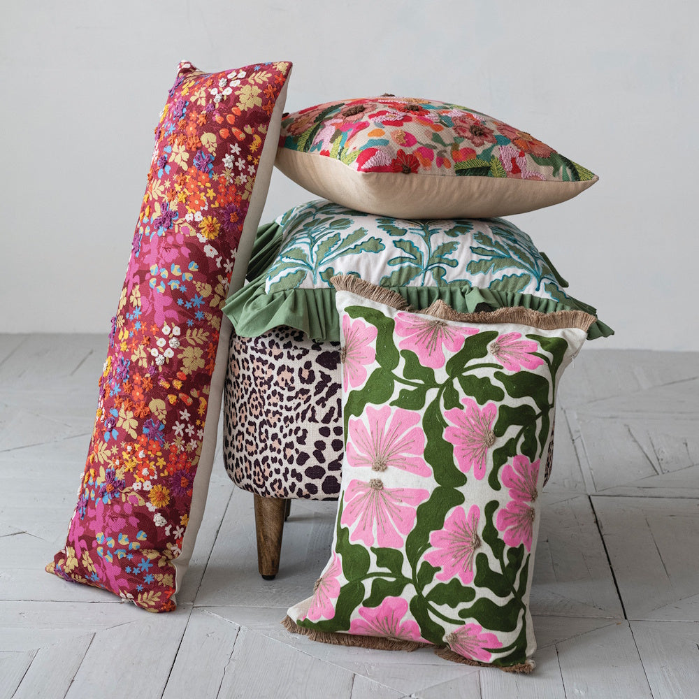 Assorted floral embroidered throw pillows and a bolster cushion stacked on a leopard print ottoman.