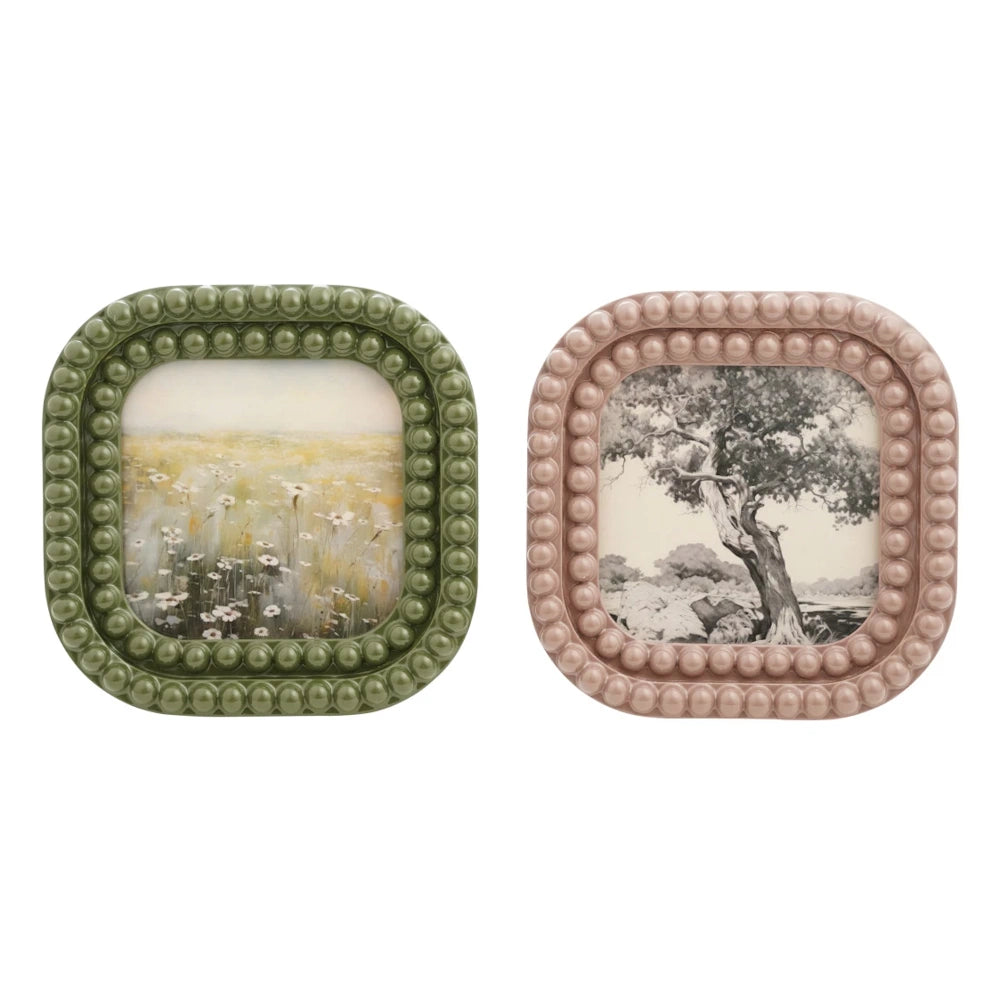 Two square resin bobbin picture frames in sage green and dusty rose pink, featuring a field and tree art print.