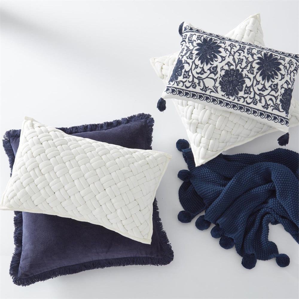 Navy and white decorative pillows with basketweave texture, floral embroidery, and a pom-pom knit throw blanket.