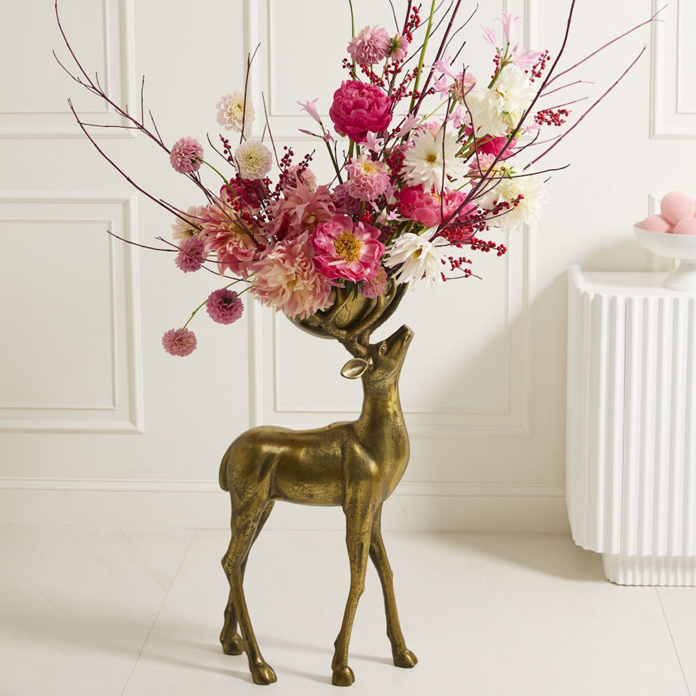 Bronze deer figurine bowl filled with vibrant pink and white flowers indoors.