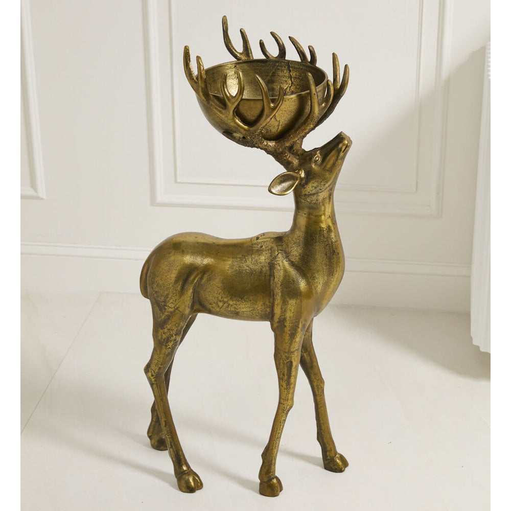 Bronze-colored deer statue with a bowl nestled in its antlers, standing on a light floor against a wall.