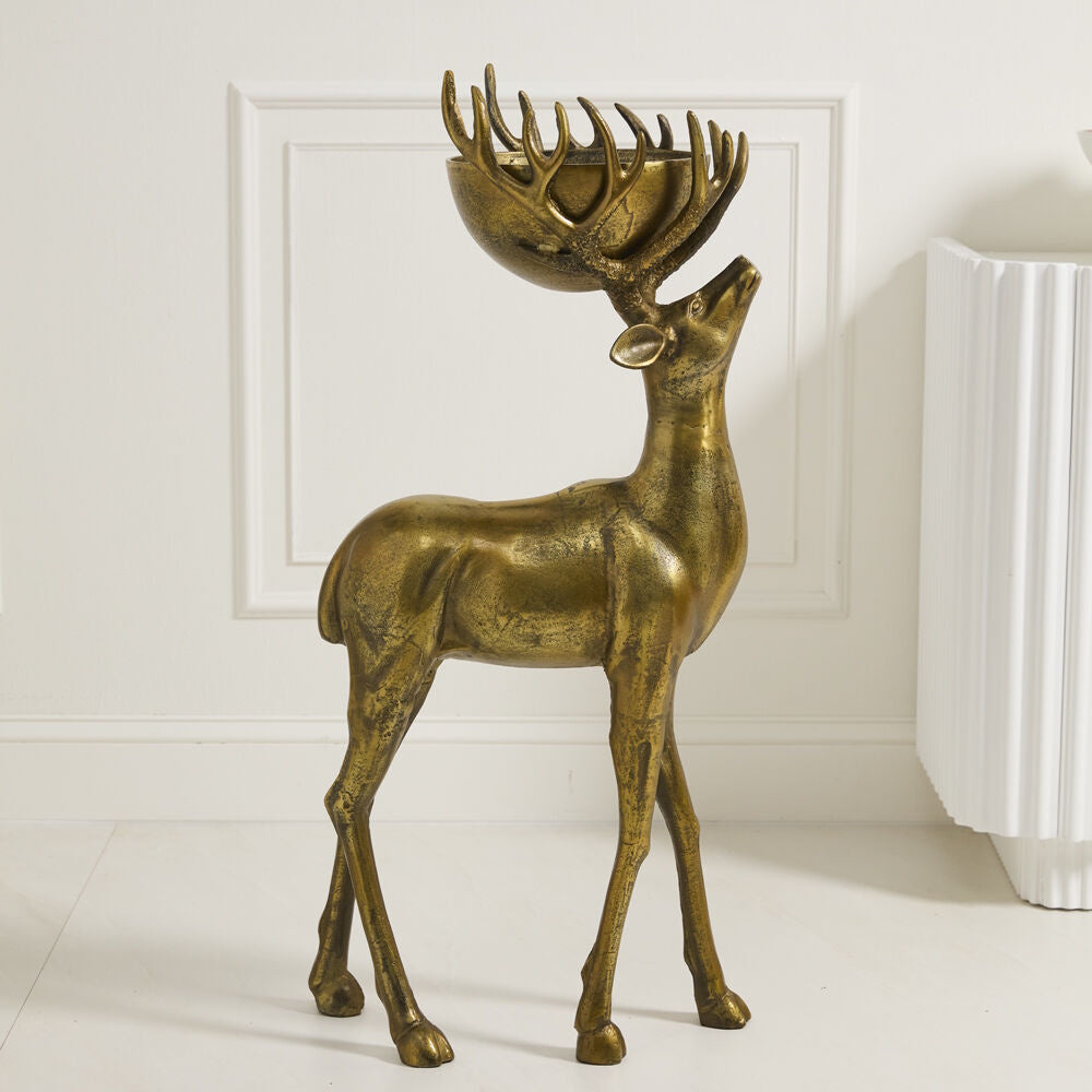 Bronze deer statue with a bowl nestled in its antlers, standing indoors against a white wall.