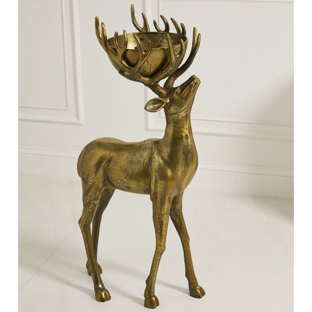Bronze deer statue with a bowl in its antlers, standing indoors against a white wall.