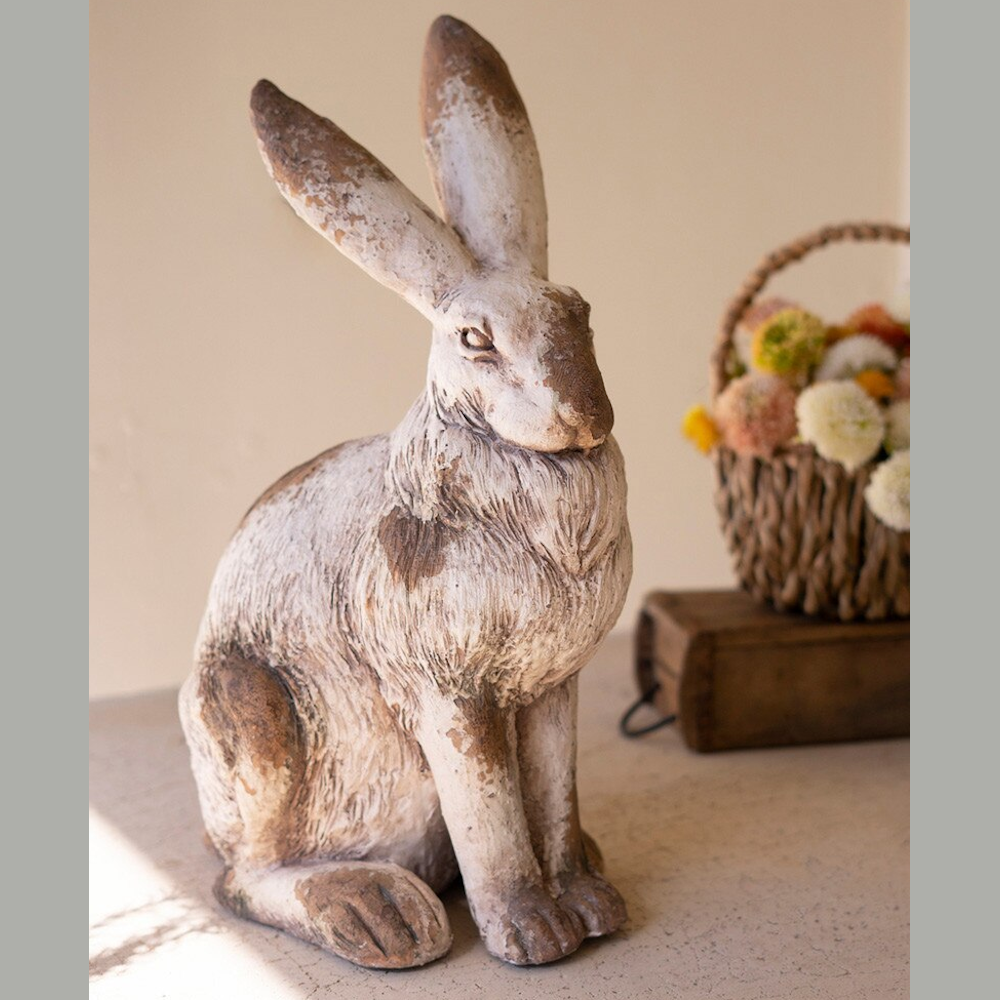 Rustic faux concrete rabbit statue with weathered brown finish and tall ears next to a small flower basket.