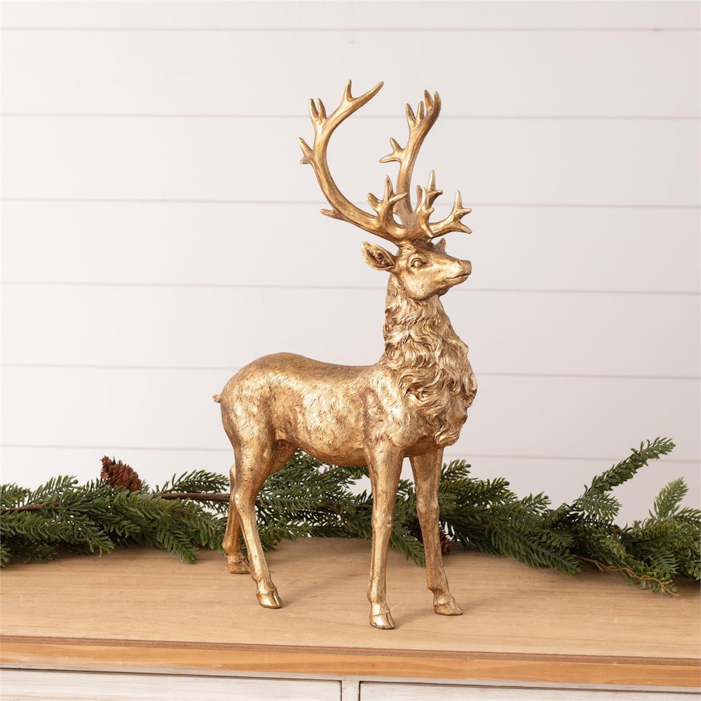 A standing gold deer figurine with large antlers, set against pine garland on a wooden surface.