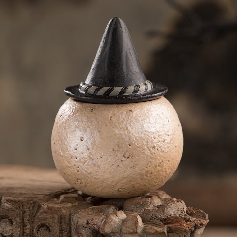 Back view of a round, textured full-moon container wearing a black witch hat lid on a rustic wood surface.