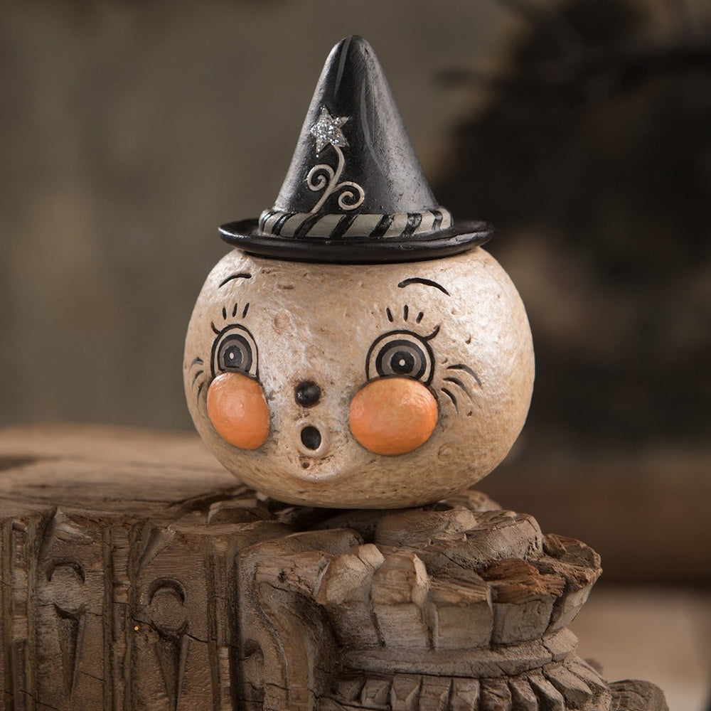 Vintage-style round moon face figurine wearing a black witch hat with a star, sitting on carved wood.