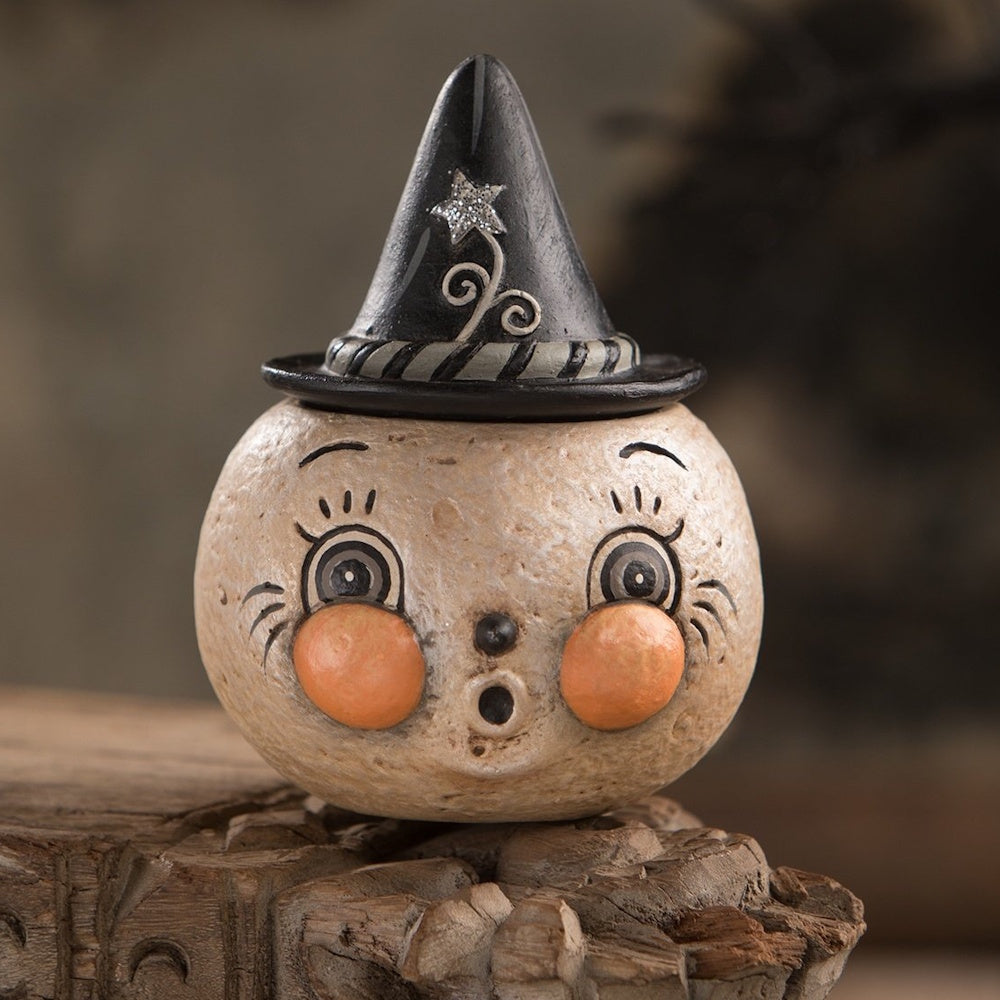 A vintage-style, round moon face container wearing a black witch hat with a silver star on a rustic wood ledge.