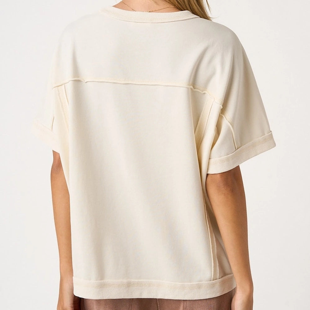 The back of a person wearing an off-white, loose-fitting short-sleeve shirt with exposed seam detailing.