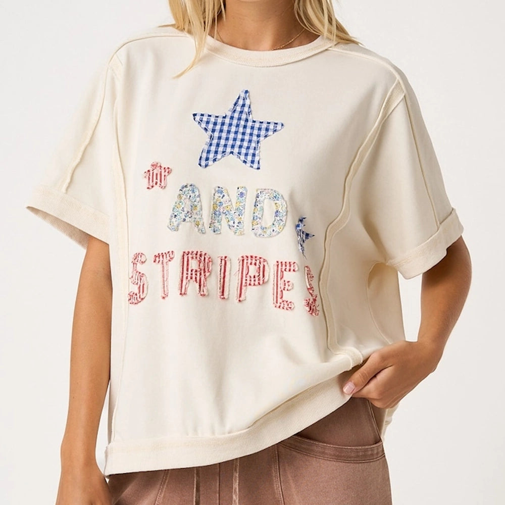 An off-white short-sleeve sweatshirt featuring patchwork text that reads "AND STRIPES" with a blue star.