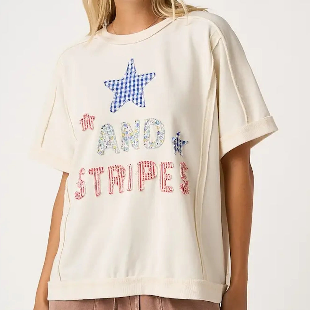 Cream short-sleeve sweatshirt with patterned patchwork letters and stars spelling "AND STRIPES".