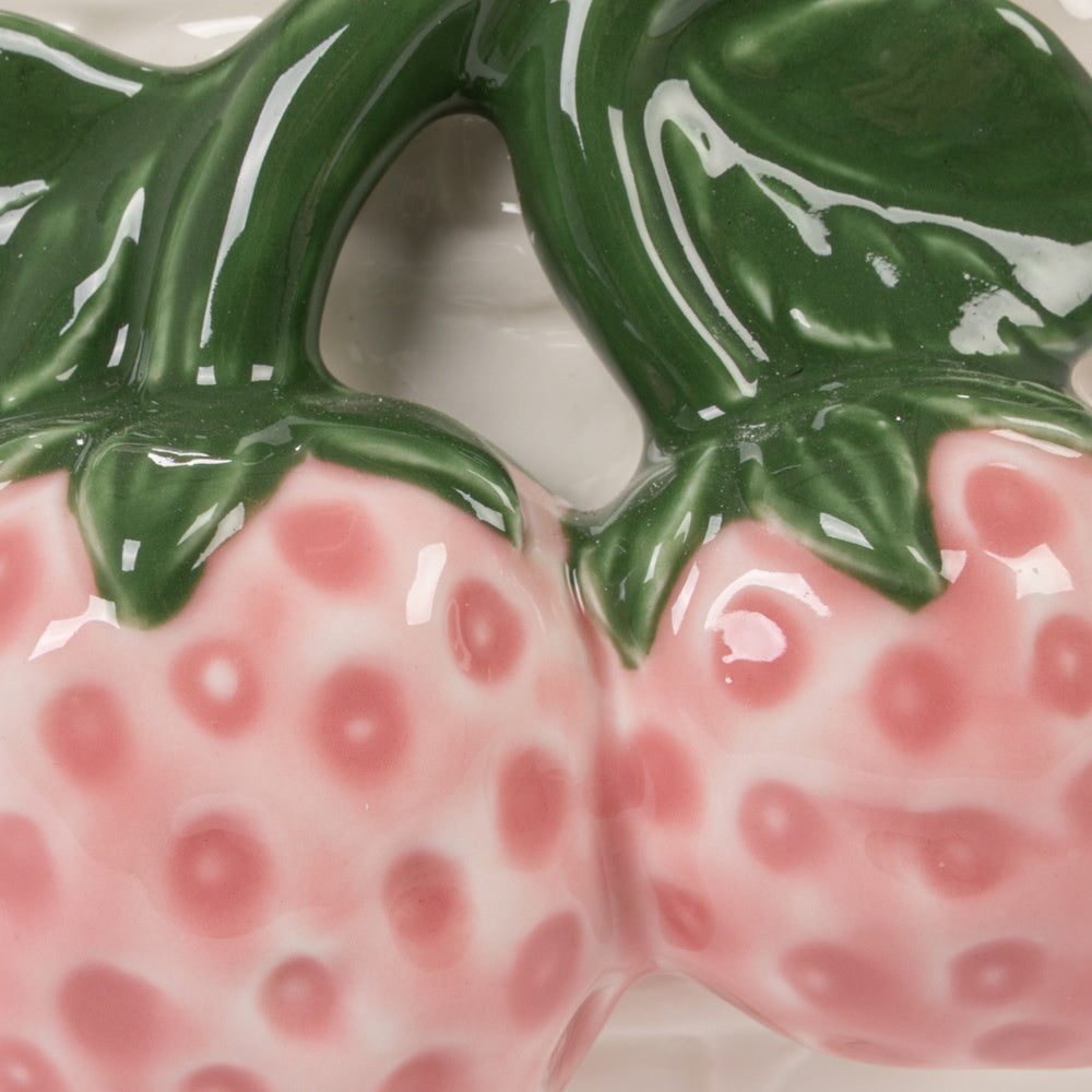 Close-up of pink and white ceramic strawberries with green glazed leaves on a stoneware basket-shaped container.