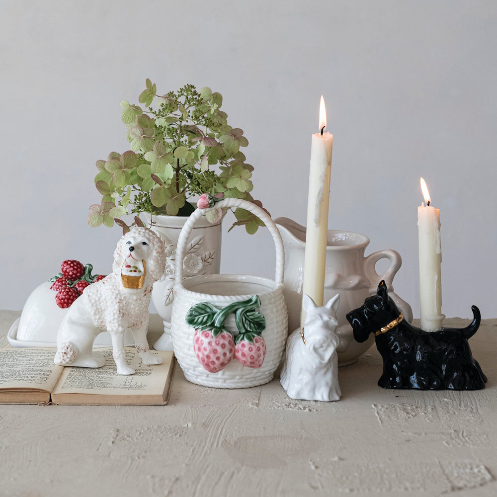 Ceramic strawberry basket, poodle and terrier figurines, and lit candles in a cottagecore-style decorative tabletop display.