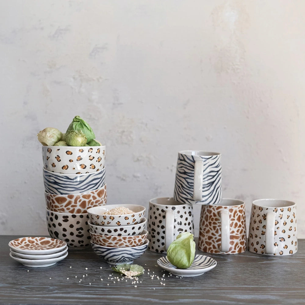 Hand-painted animal print ceramic mugs and bowls featuring leopard, zebra, and giraffe patterns on a rustic wooden table.
