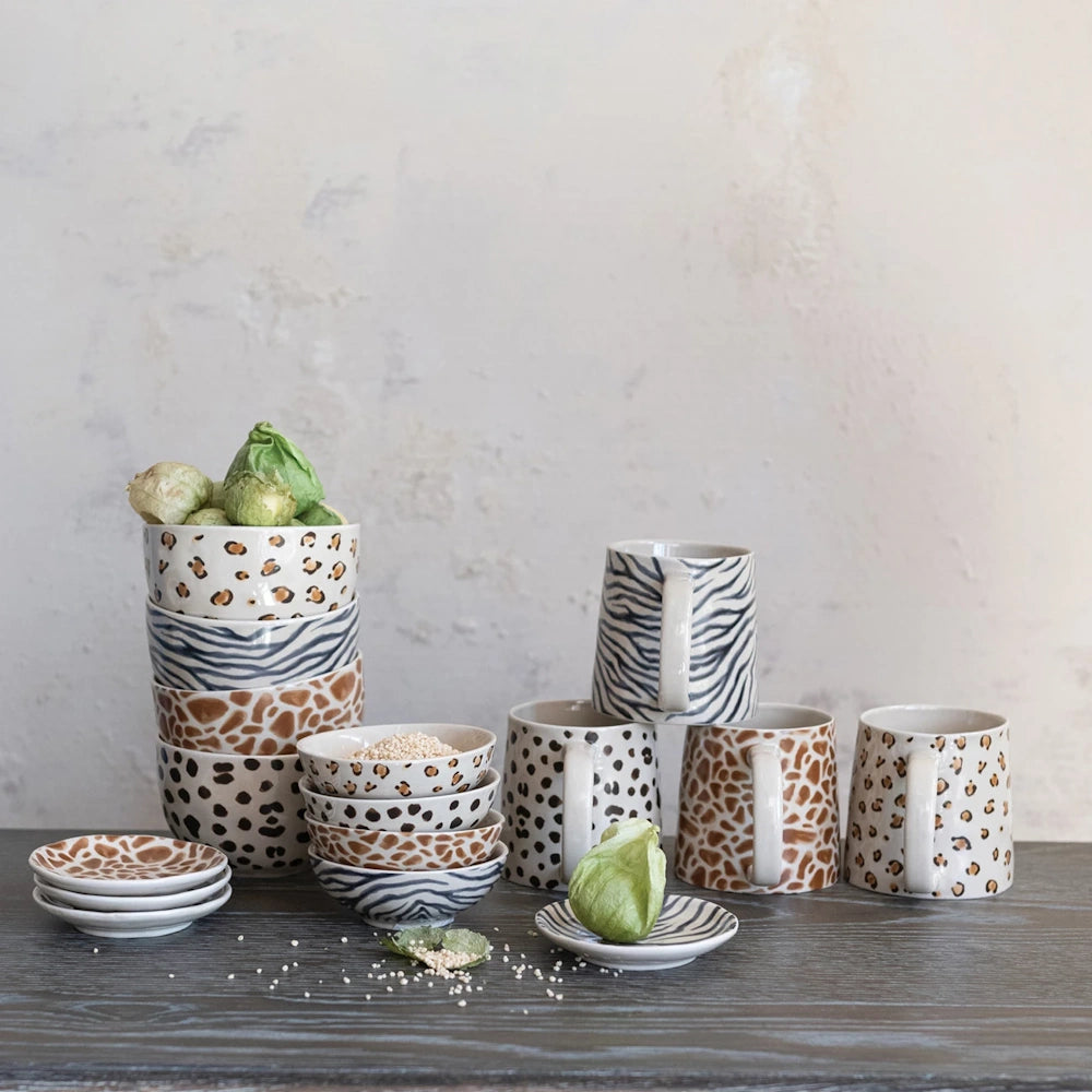 Animal print ceramic dinnerware set including mugs, bowls, and plates with leopard, zebra, and giraffe patterns.