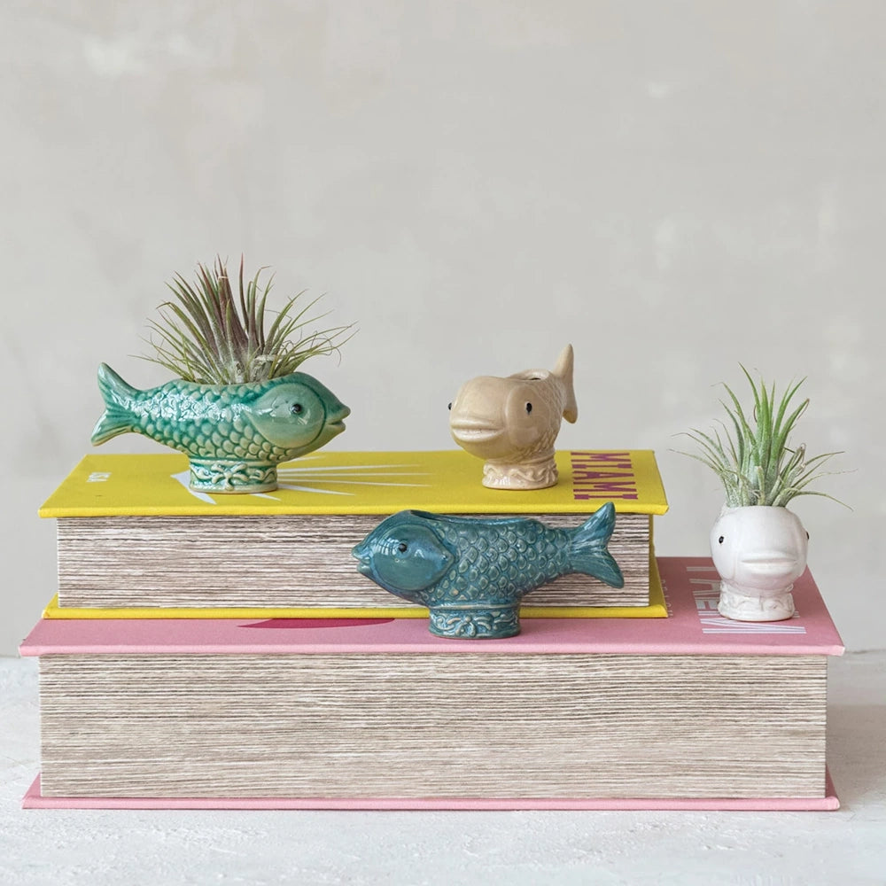 Small fish-shaped pottery planters for air plants displayed on yellow and pink coffee table books.