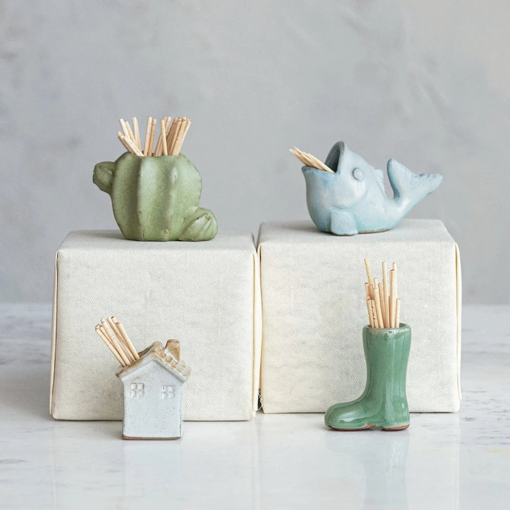 Four decorative mini stoneware toothpick dispensers including a green cactus and blue whale on a marble surface.