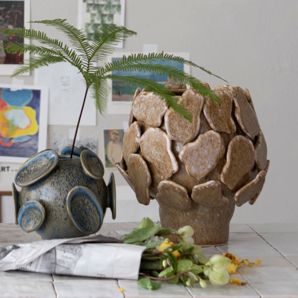 Brown footed planter with a 3D textured design next to a blue spherical vase holding a fern frond.