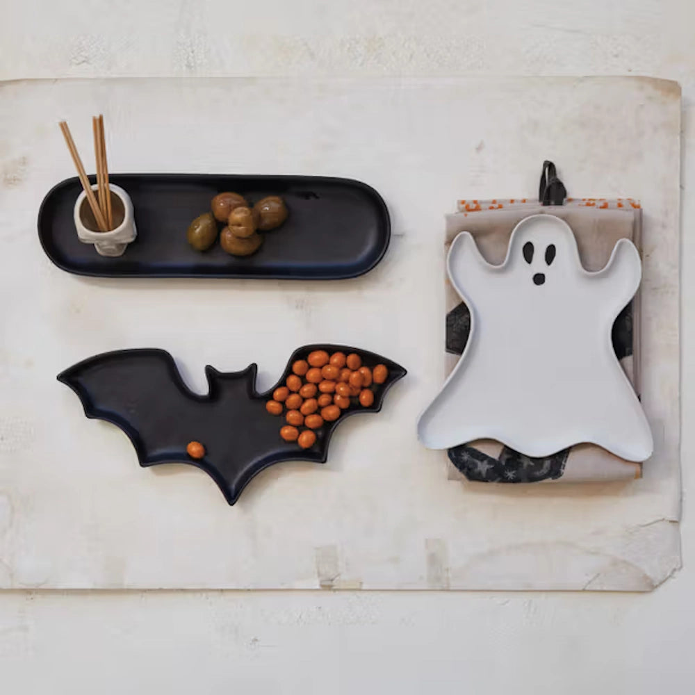 White ghost plate next to a black bat-shaped tray filled with orange snacks on a textured background.