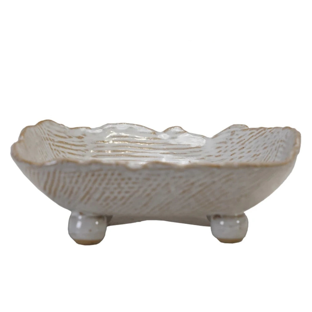 Side view of an organic-shaped white ceramic footed dish featuring a textured, ribbed pattern and wavy edges.