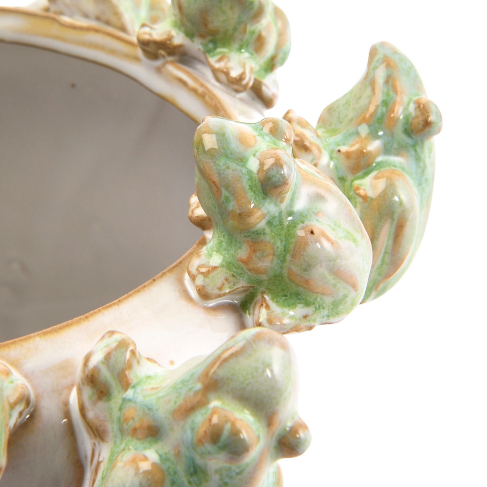 Close-up of a ceramic planter rim decorated with sculpted green and beige frogs.