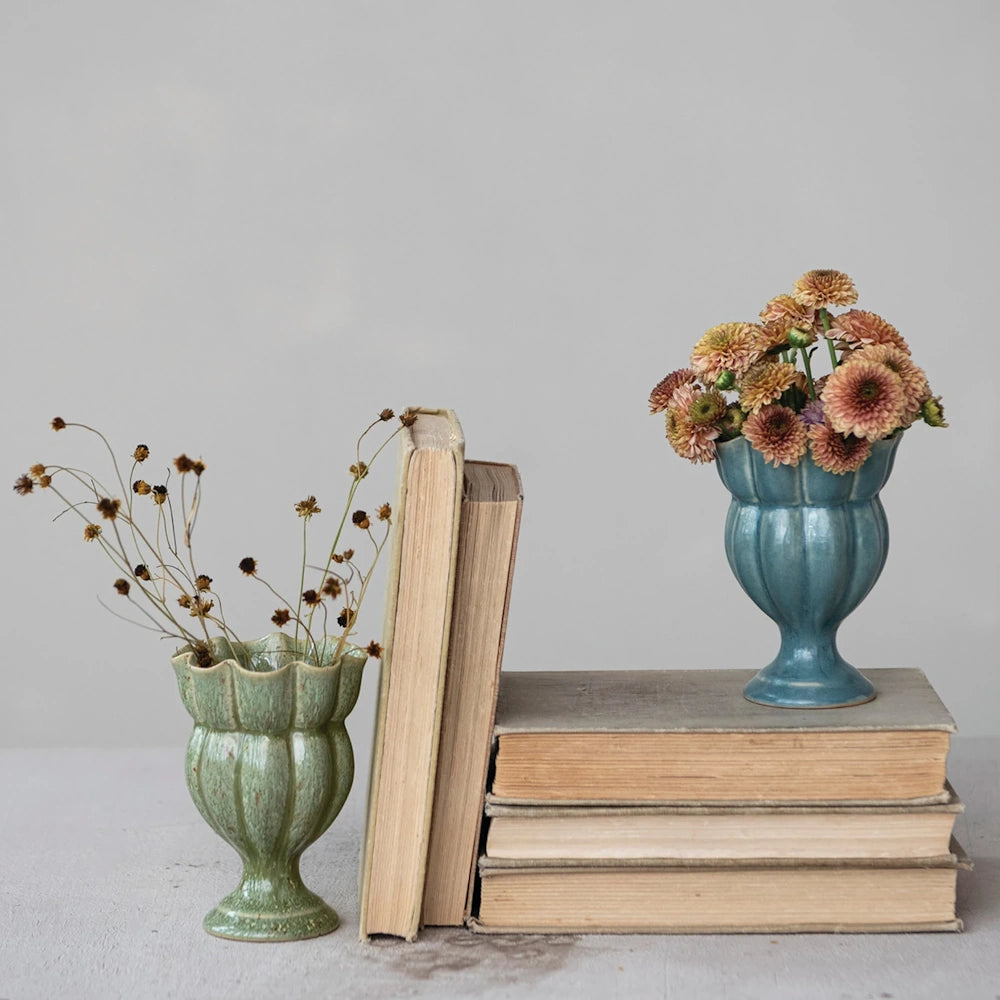Green and blue scalloped footed ceramic vases styled with flowers alongside stacked vintage books.