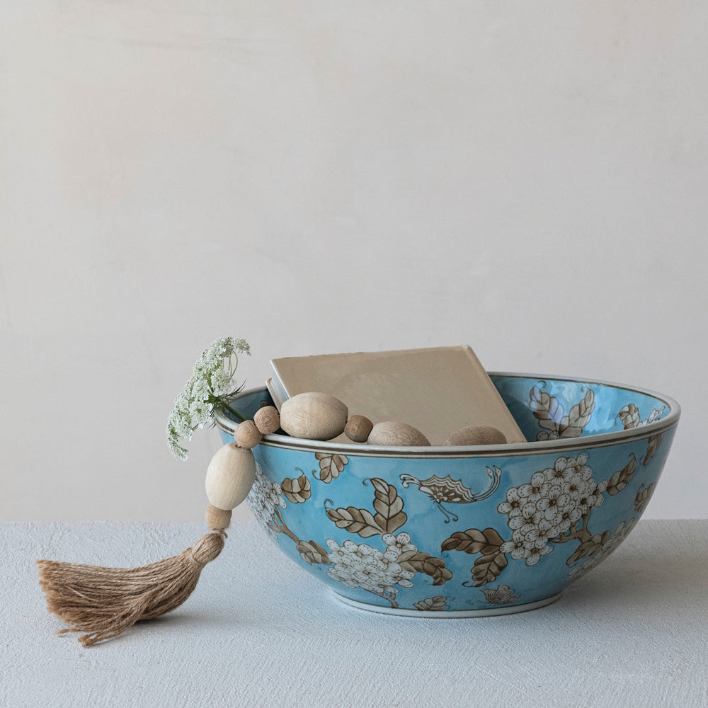 Blue stoneware bowl with white cherry blossoms and brown leaves, holding a book and wooden beads with a tassel.