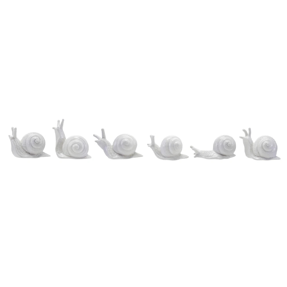Row of six white ceramic snail figurines in various poses, minimalist stoneware home decor on a white background.