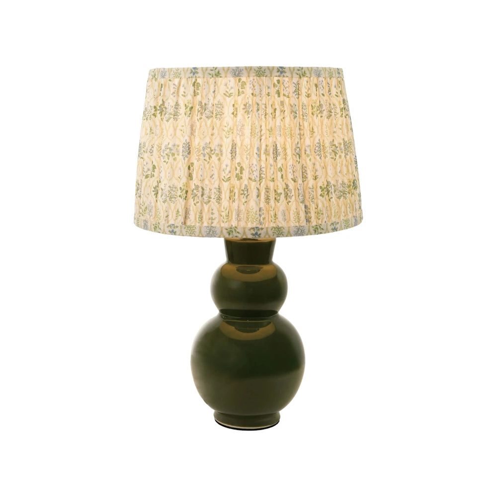 Front view of a illuminated dark green stoneware table lamp with a pleated floral fabric shade.