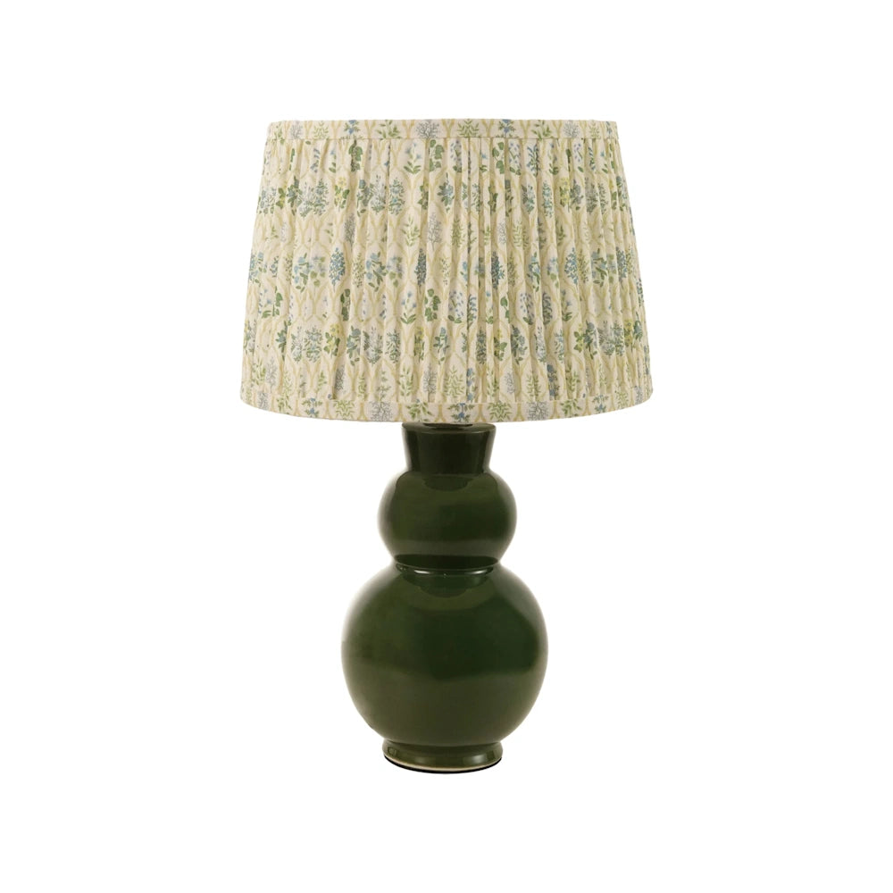 Front view of a dark green glazed stoneware table lamp with a pleated floral fabric shade.