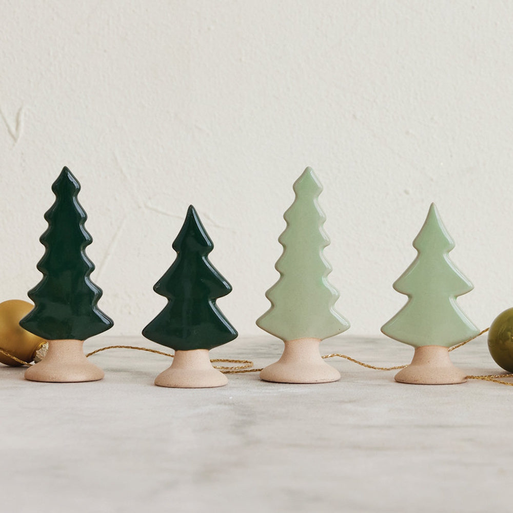 Four small ceramic Christmas tree figurines in dark and light green shades with unglazed bases.