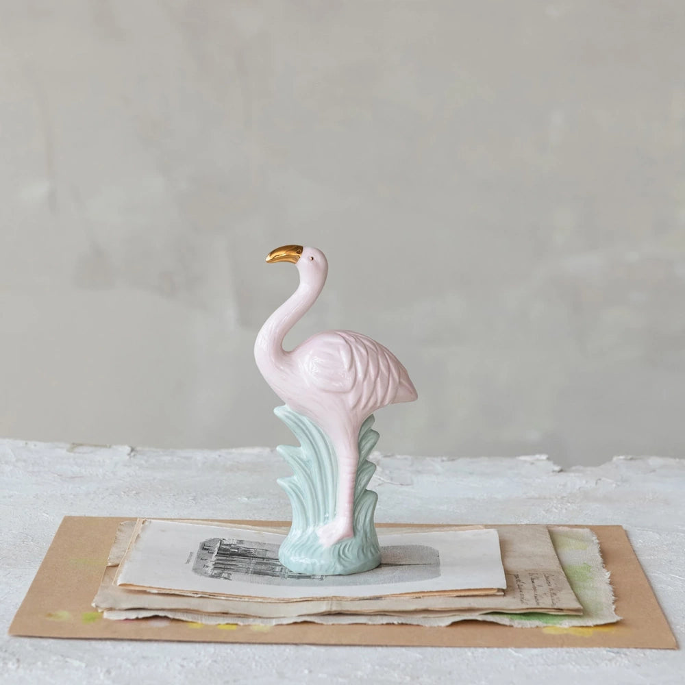 Pink ceramic flamingo figurine with gold beak on vintage paper stack, elegant tropical home decor accent.