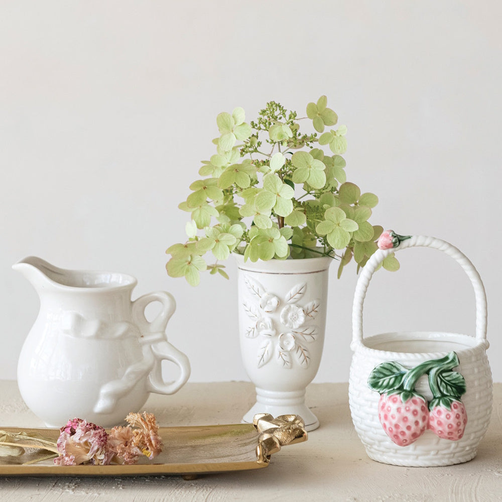Stoneware vintage reproduction footed vase with green flowers alongside a ceramic pitcher and basket.
