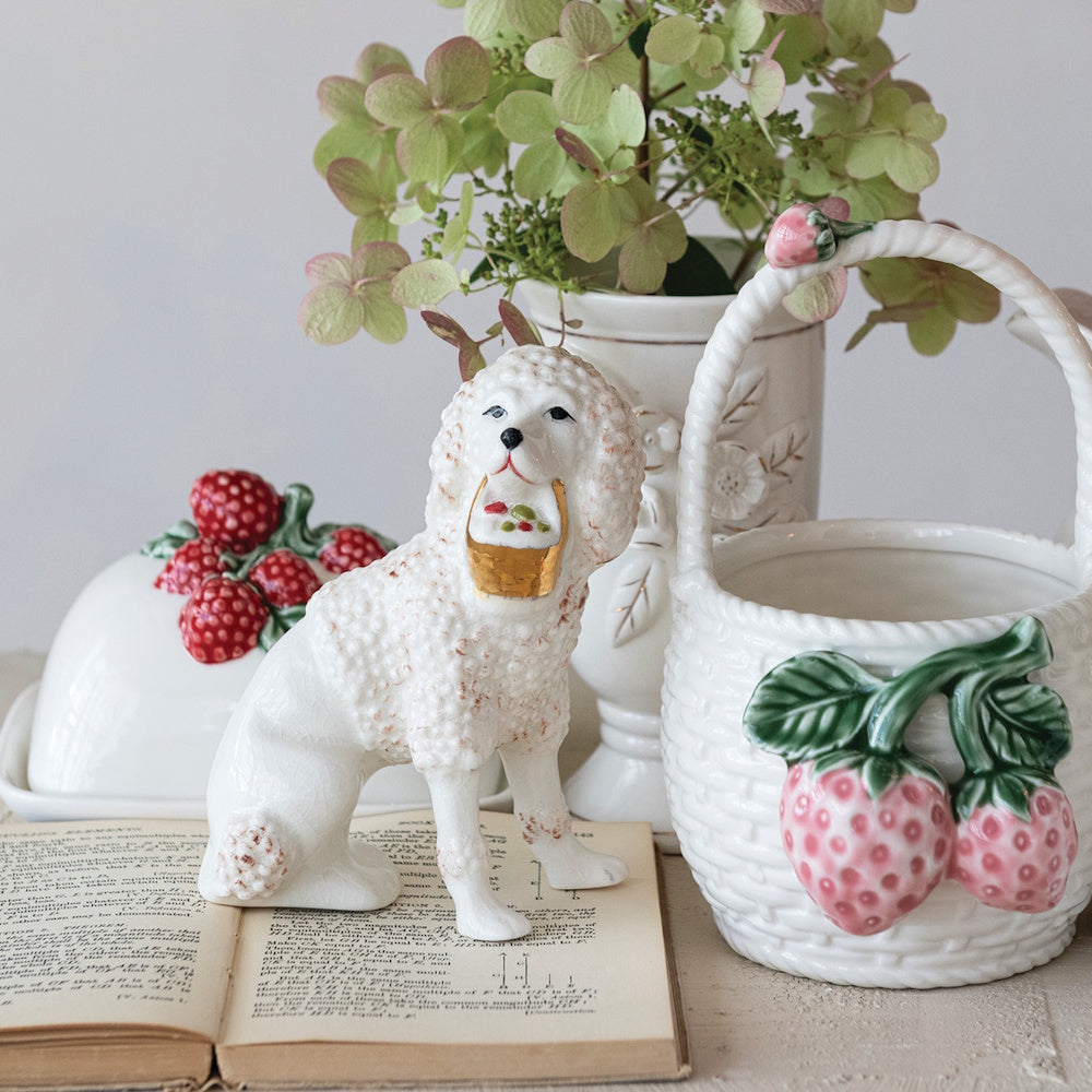 Vintage reproduction Staffordshire poodle figurine on an open book next to strawberry ceramic tableware.