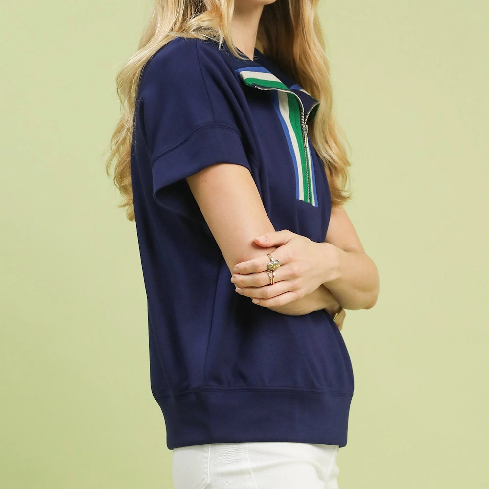 Navy blue short-sleeve half-zip knit top with green and white striped collar detail, worn with white pants.