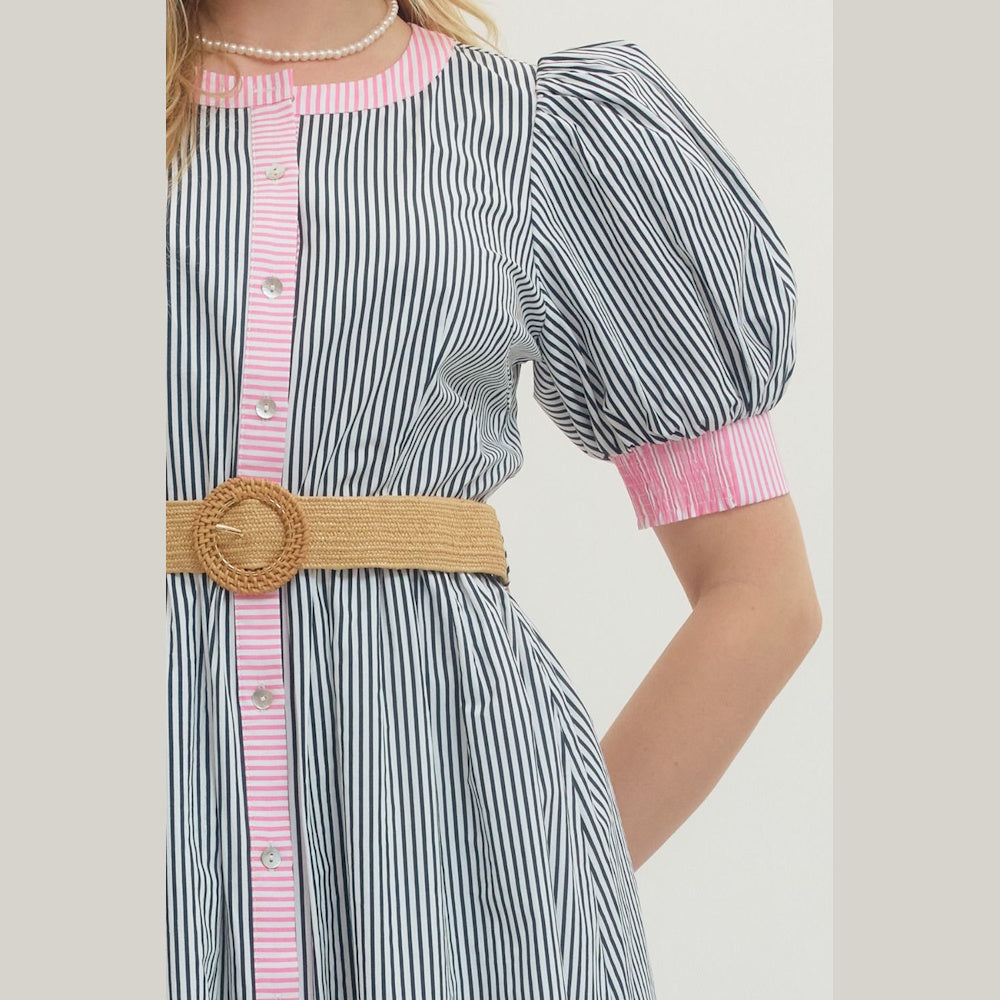 A woman in a navy striped dress with pink seersucker trim, puff sleeves, a woven raffia belt, and pearl necklace.