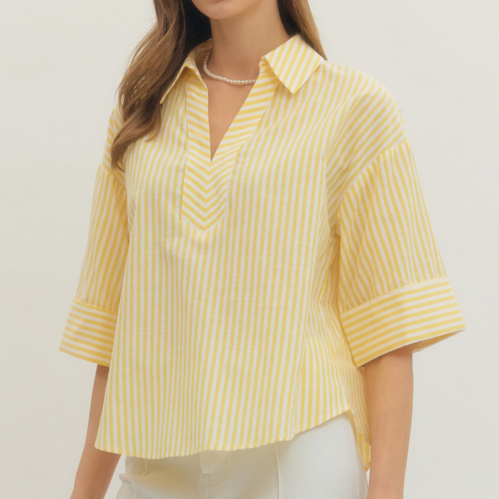 A woman wearing a yellow and white striped split V-neck top with three-quarter sleeves and a pearl necklace.