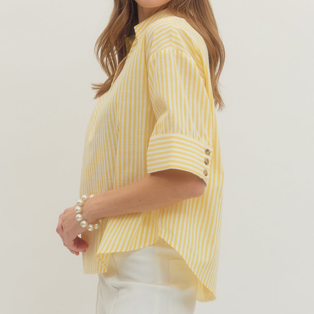 Side view of a woman wearing a yellow and white striped split V-neck top with three-quarter sleeves.
