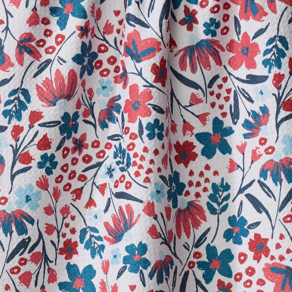 Close-up of fabric with a small floral print featuring red and blue blossoms on a white background.