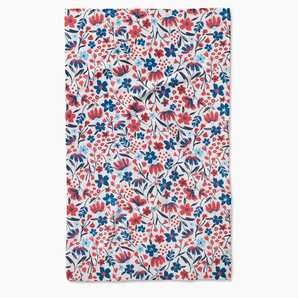 A tea towel featuring a repeating allover floral pattern with red, navy blue, and light blue blossoms.